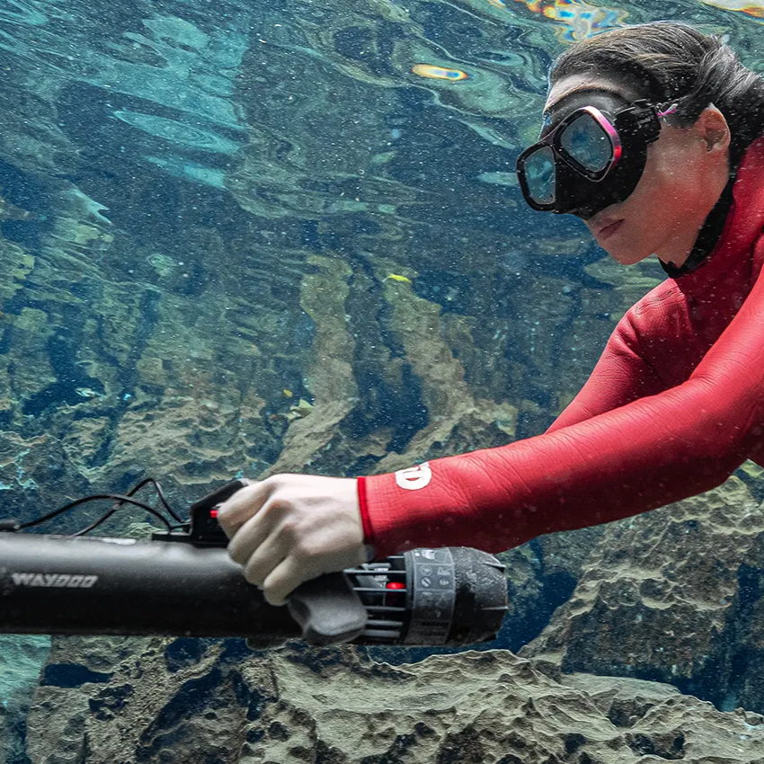 Person in a red wetsuit holding a subnado underwater with rocky and aquatic background