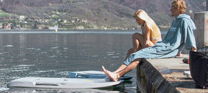 Two people sitting on a dock by a lake with mountains in the background